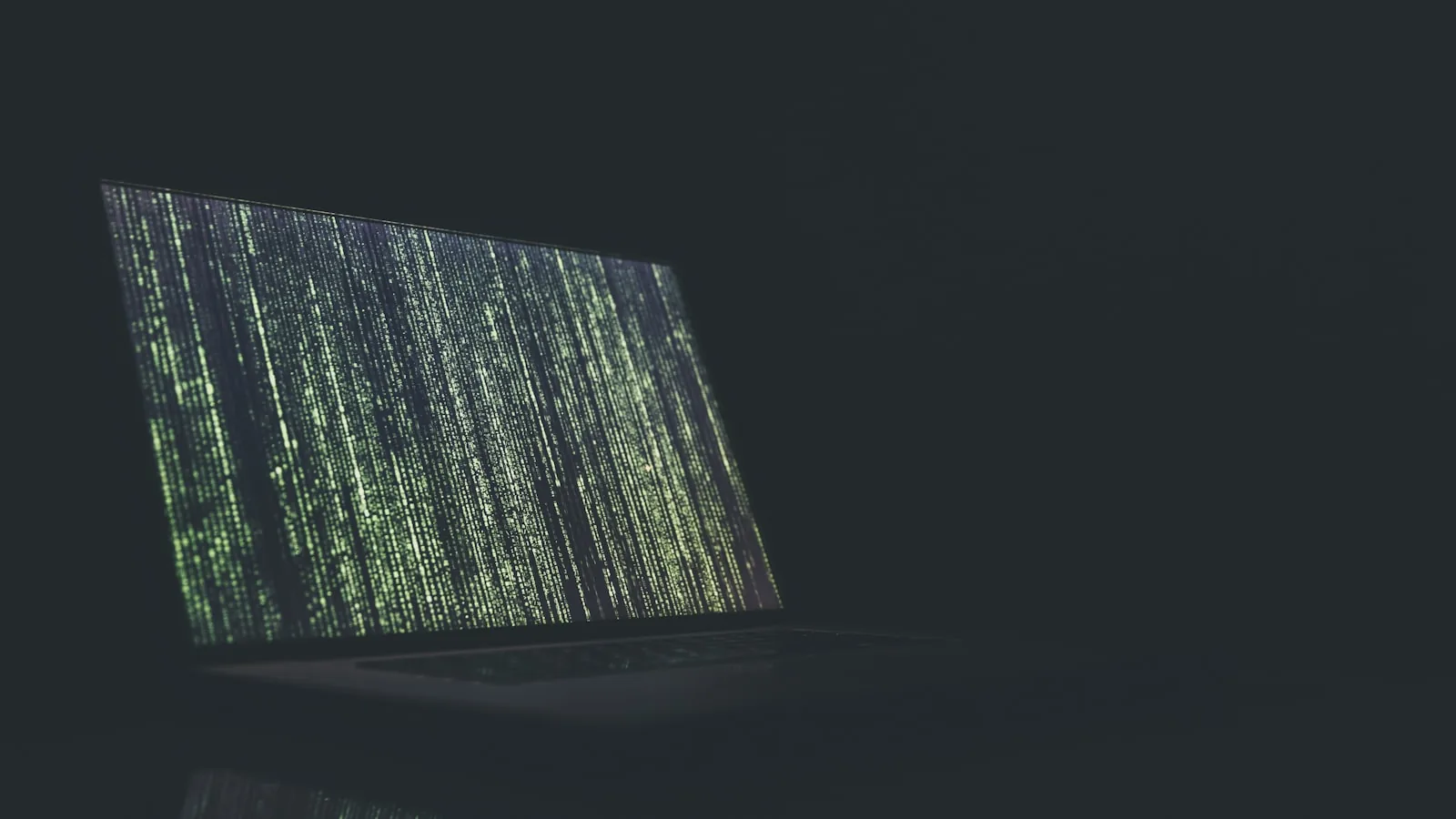 Portátil en la penumbra con líneas de código verde en la pantalla