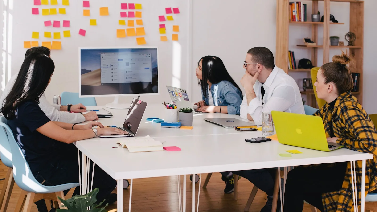 Un equipo de personas trabajando con portátiles en una mesa con notas adhesivas